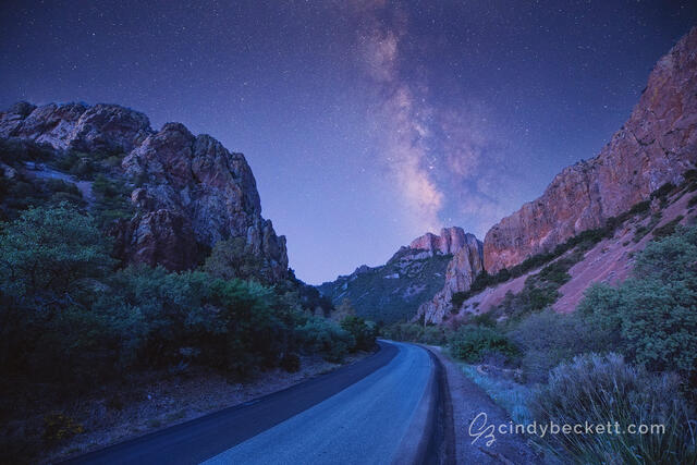 The Milky Way rises above the mountain peaks and canyon walls of the road leading into Chisos Basin in Big Bend National Park.