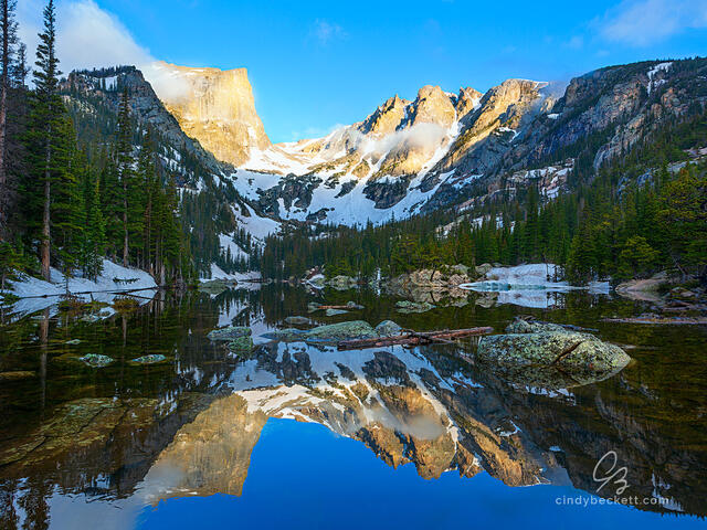 A calm and glass-like Dream Lake reflects Hallett Peak and Flat Top mountain on an early summer morning.