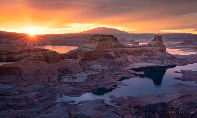 A cloudy and colorful sunrise scene over red rock canyon walls and formations surrounded by the waters of Lake Powell.